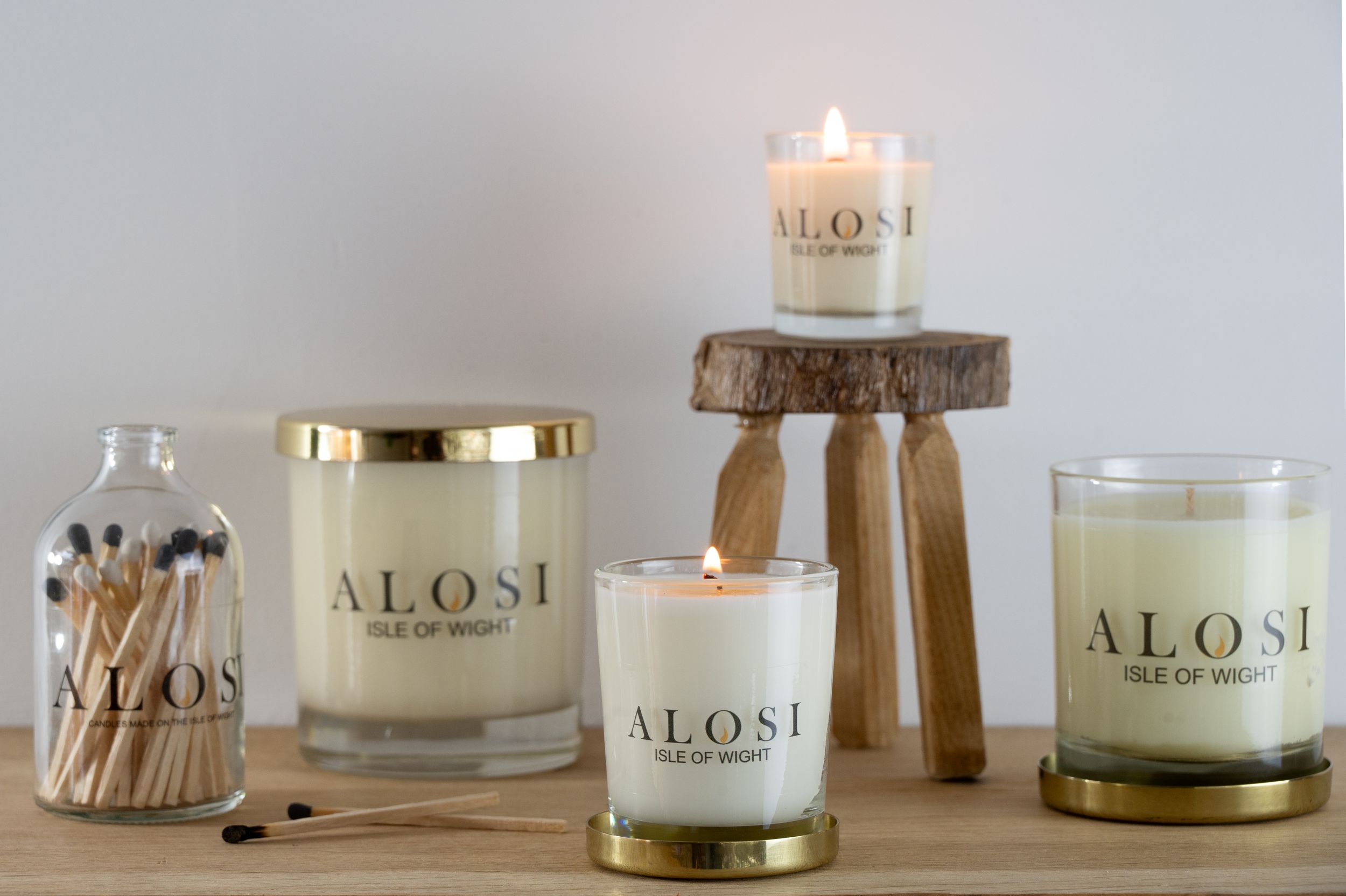 Alosi branded candles displayed on wooden stands with a jar of matches creating a cozy home decor setting.