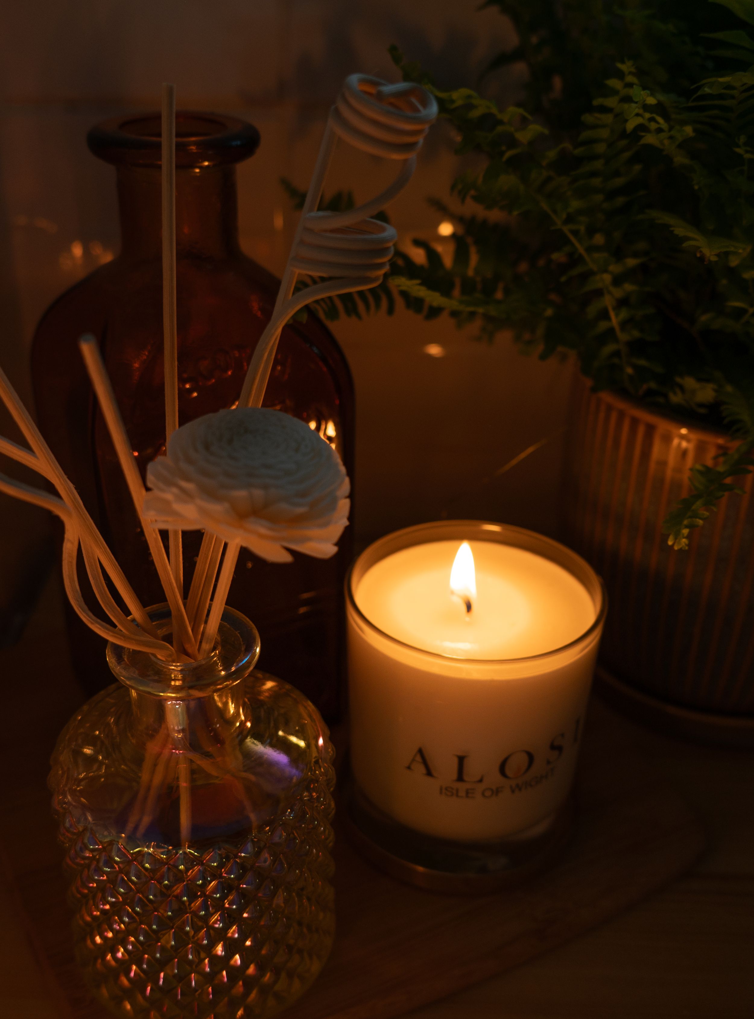 A lit white candle glows warmly in a glass jar against a dark background with decorative elements.