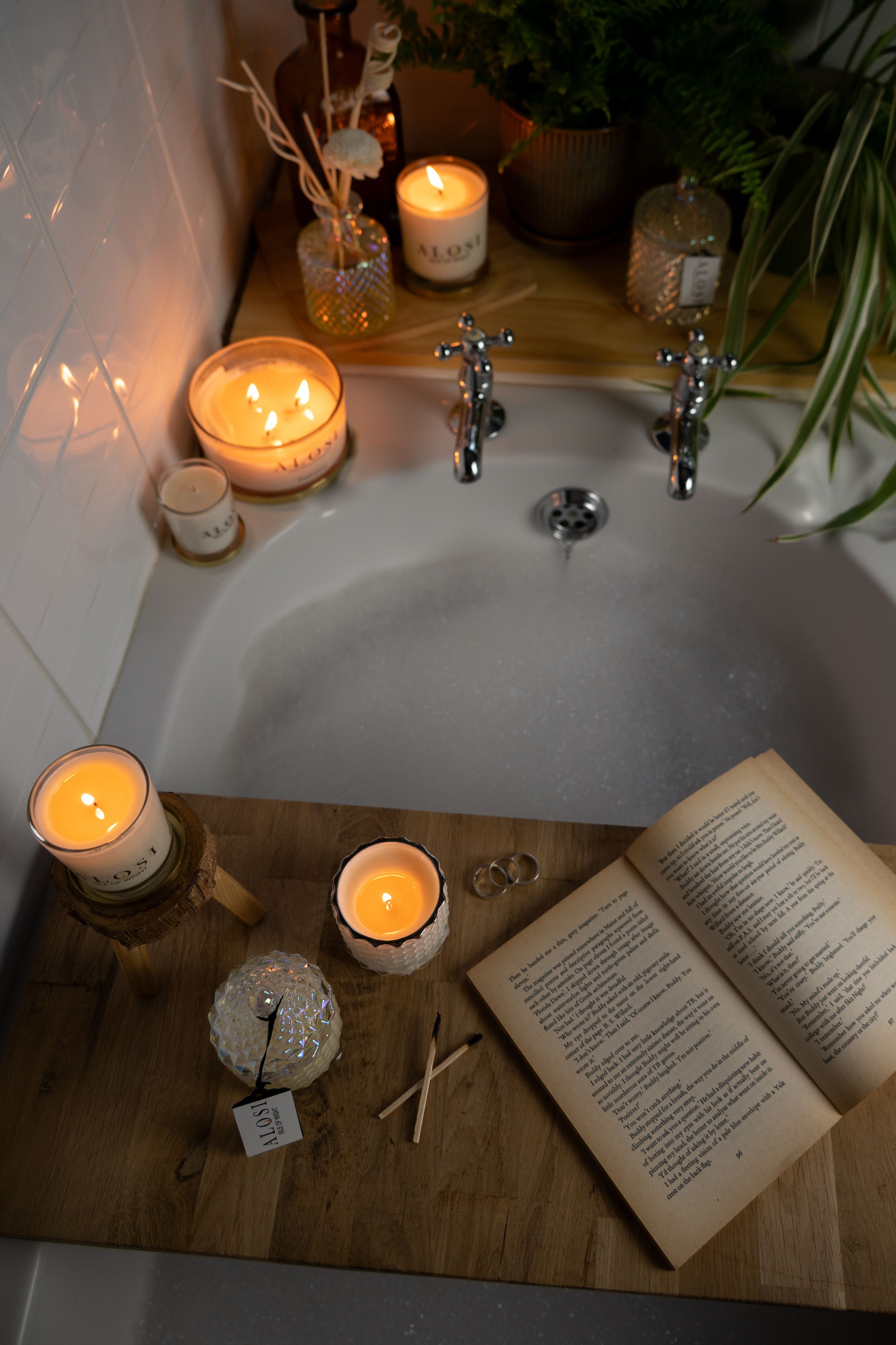 An open book illuminated by candlelight sits on a rustic wooden table with decorative glass elements.