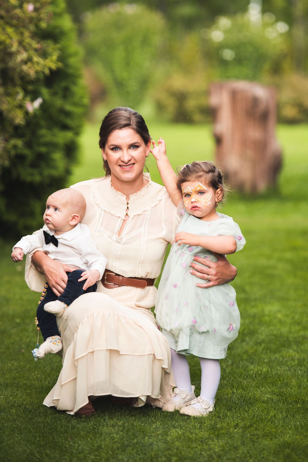 Family portrait session on lush grass showing tender moments between parent and children in vintage-style outfits.