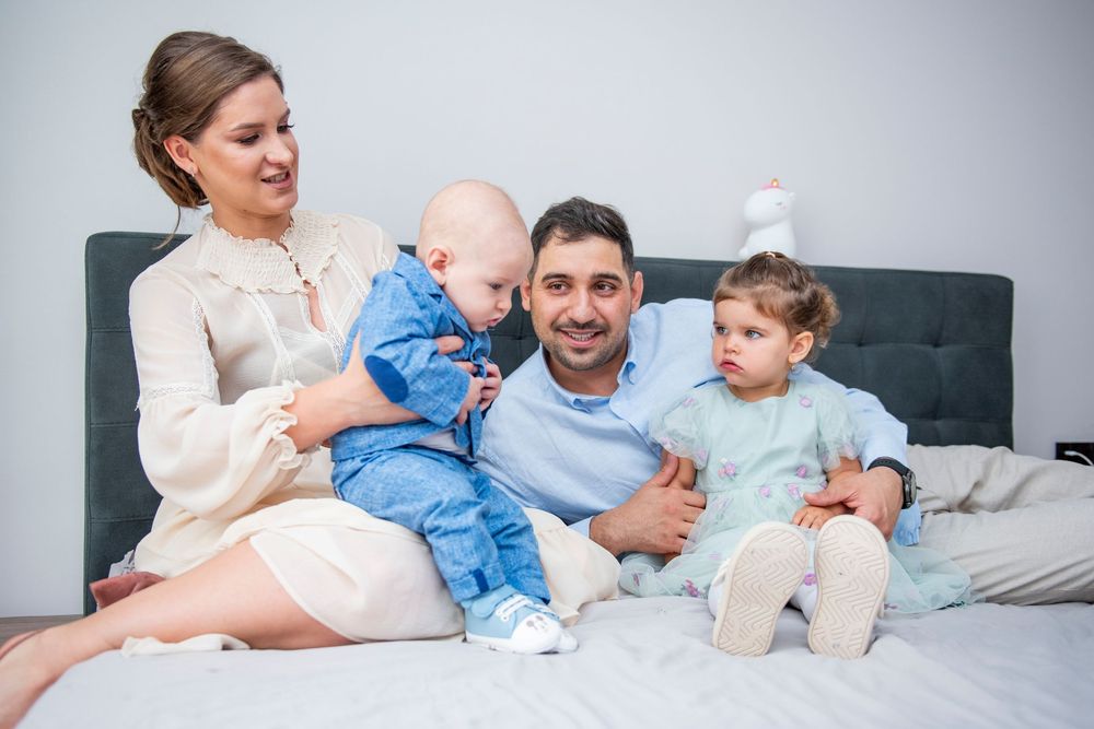 Family members in light colored clothing relaxing together on a gray couch at home.