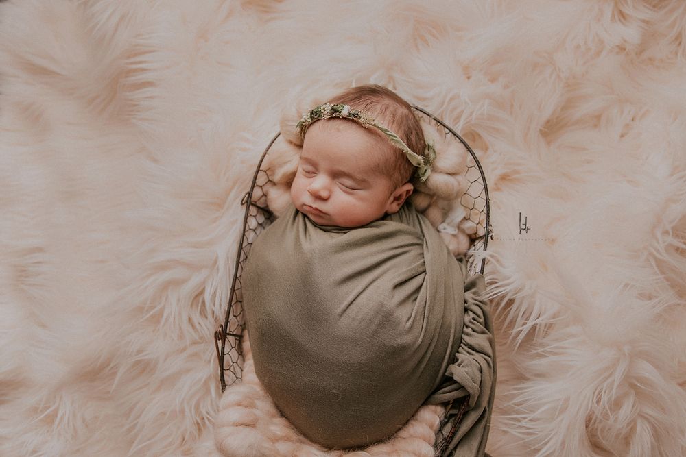 Newborn baby wrapped in soft beige fabric sleeps peacefully during professional photo session.