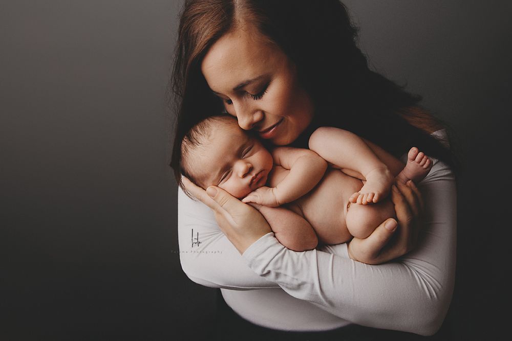 A tender moment captured between mother and newborn baby in soft black and white tones.