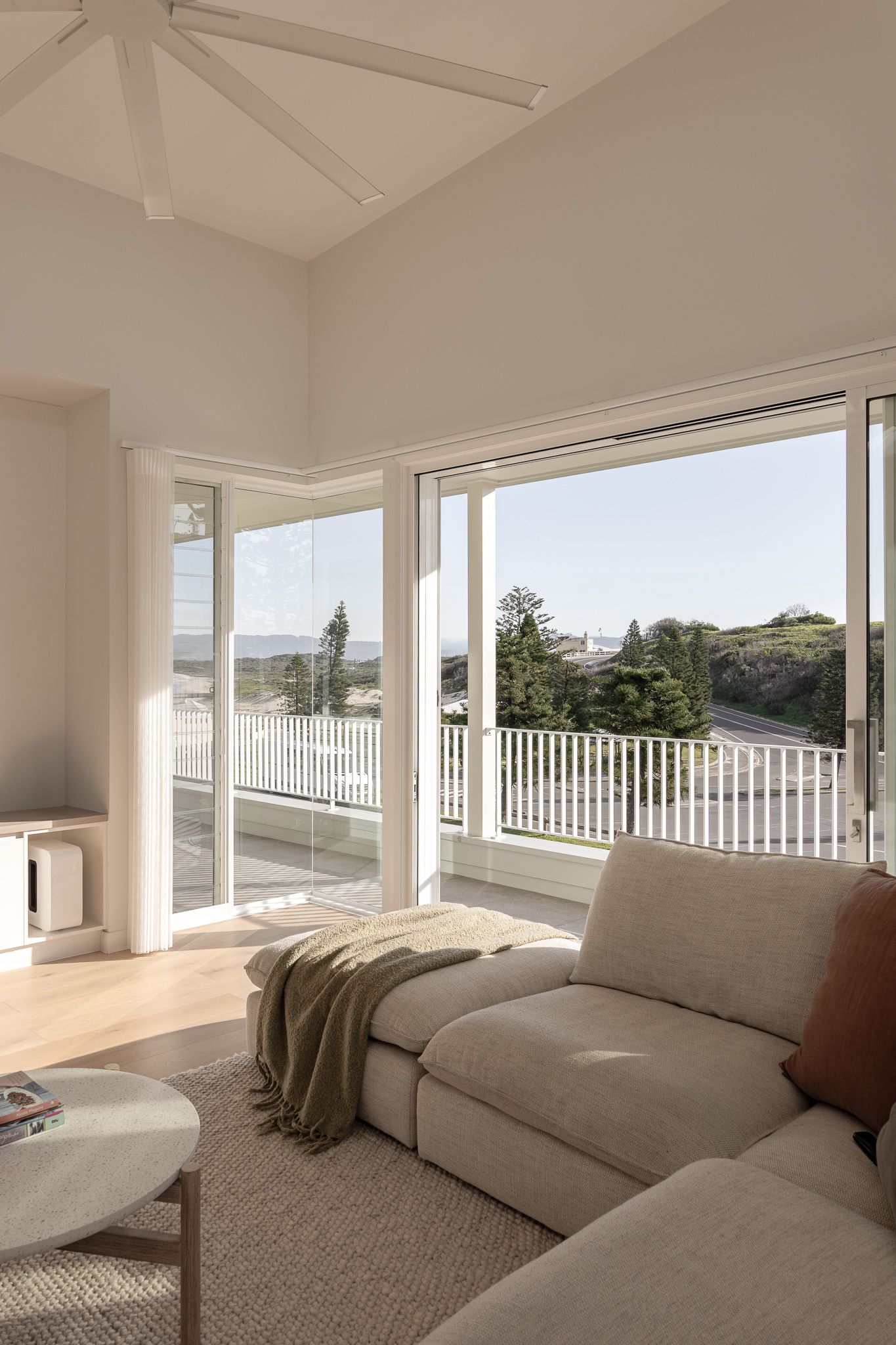 Modern living room with panoramic windows, white walls, and a comfortable gray sectional sofa overlooking an outdoor view.