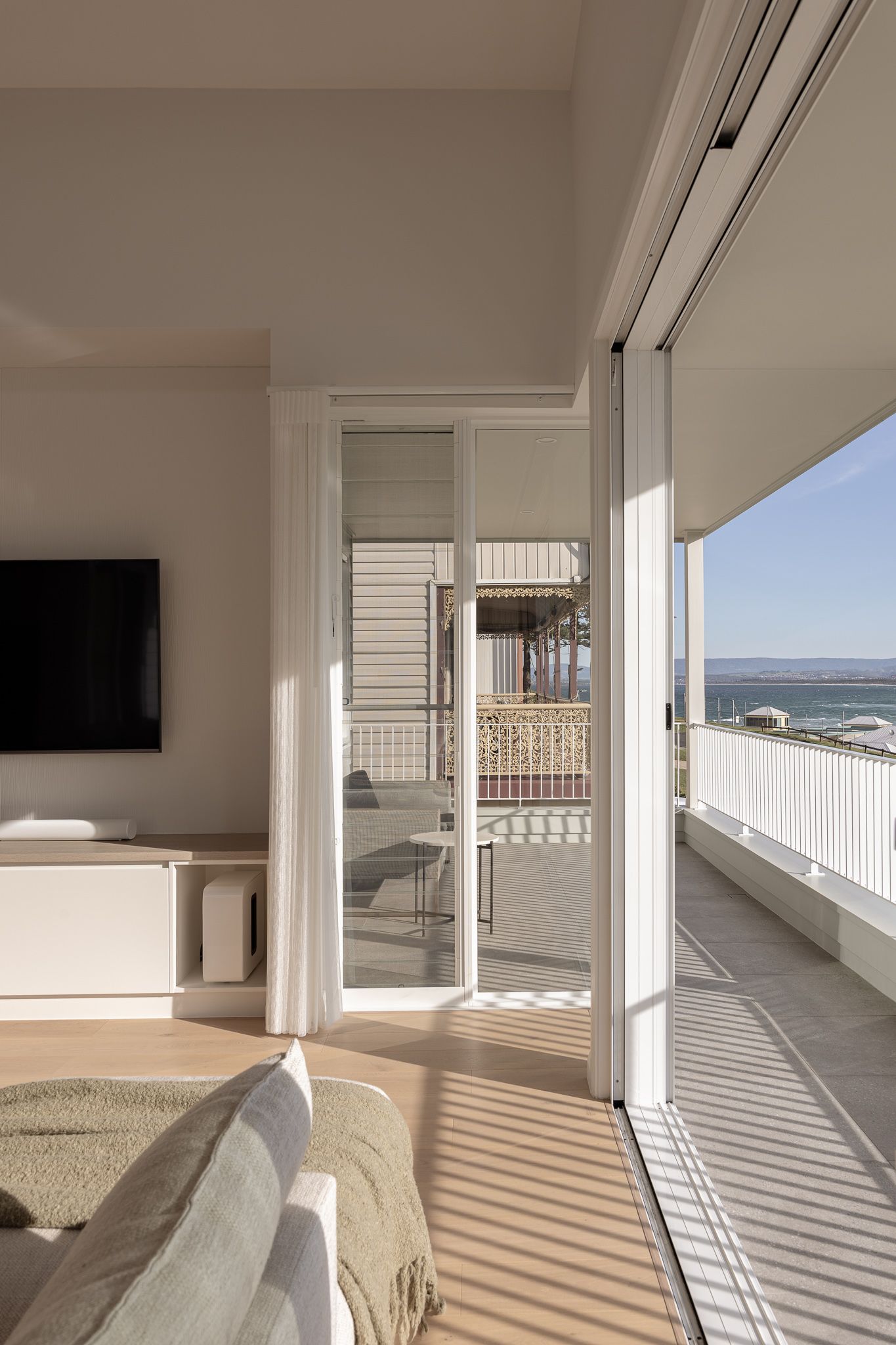 Modern beachfront living room with white walls and dramatic shadow patterns cast through large windows.