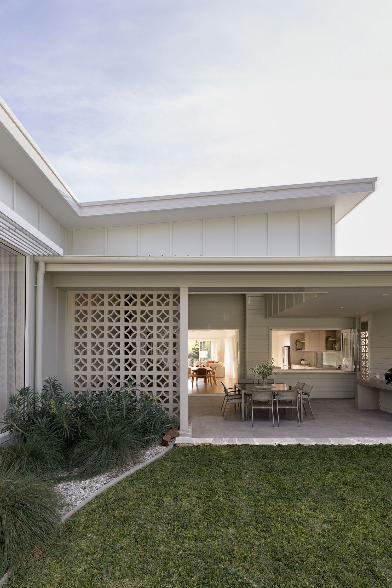 Modern white mid-century house exterior features decorative concrete blocks and landscaped lawn under cloudy skies.