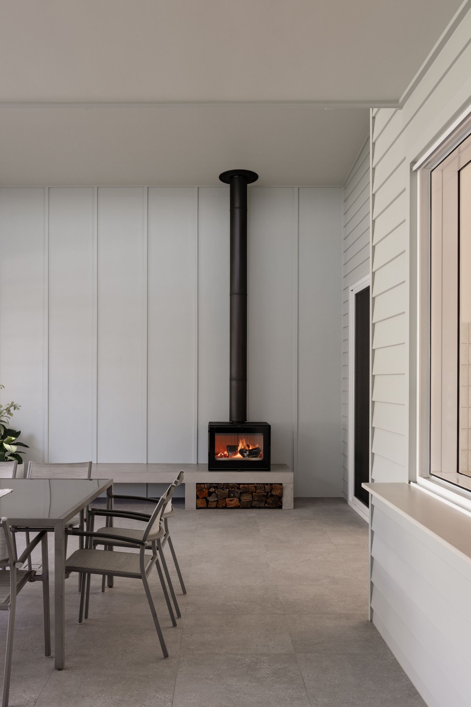 Modern patio with white walls features a sleek black fireplace and minimalist outdoor furniture on concrete flooring.