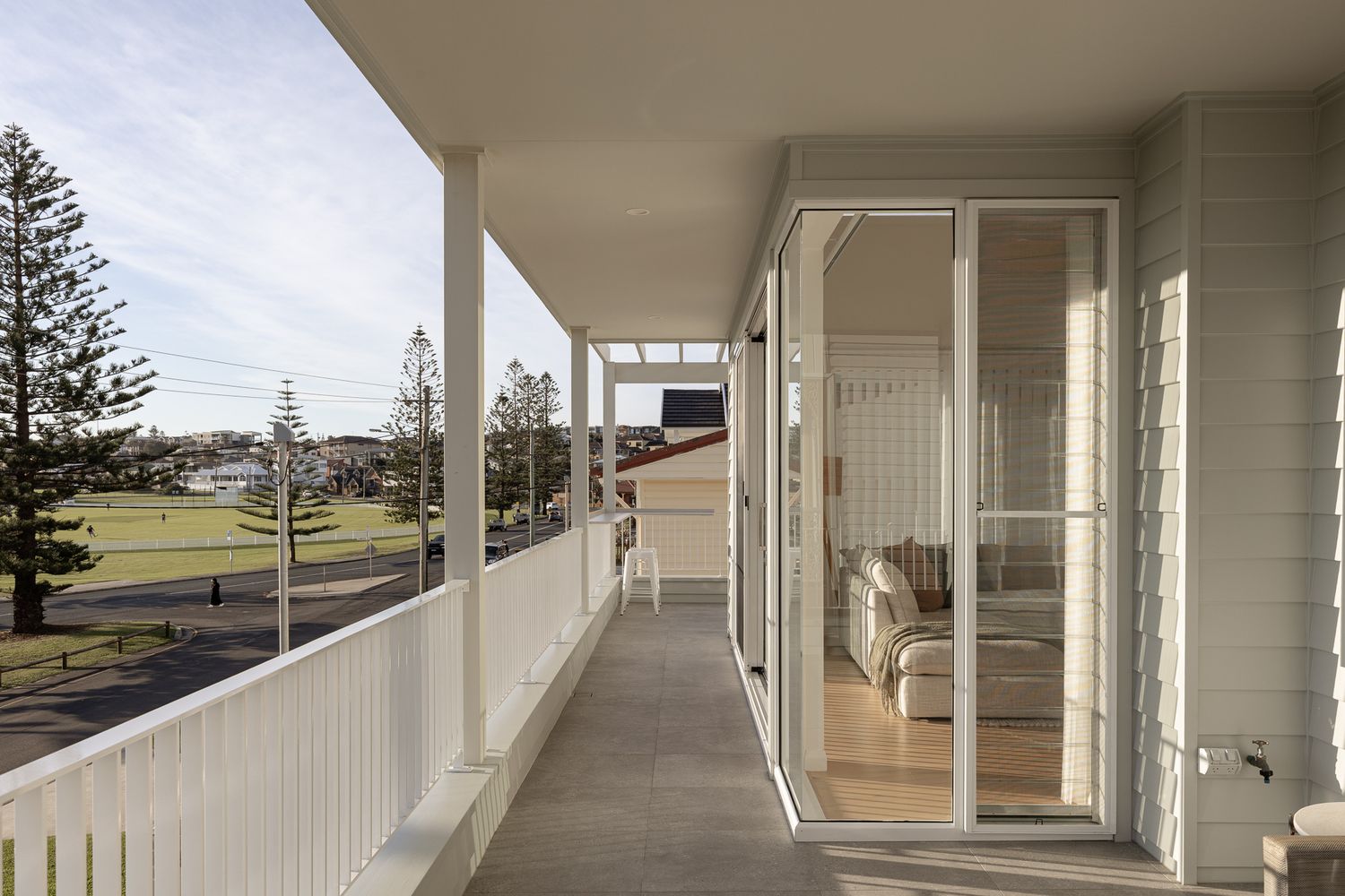 Modern white architectural colonnade with stone base extends along a curved path with scenic coastal views in the background.