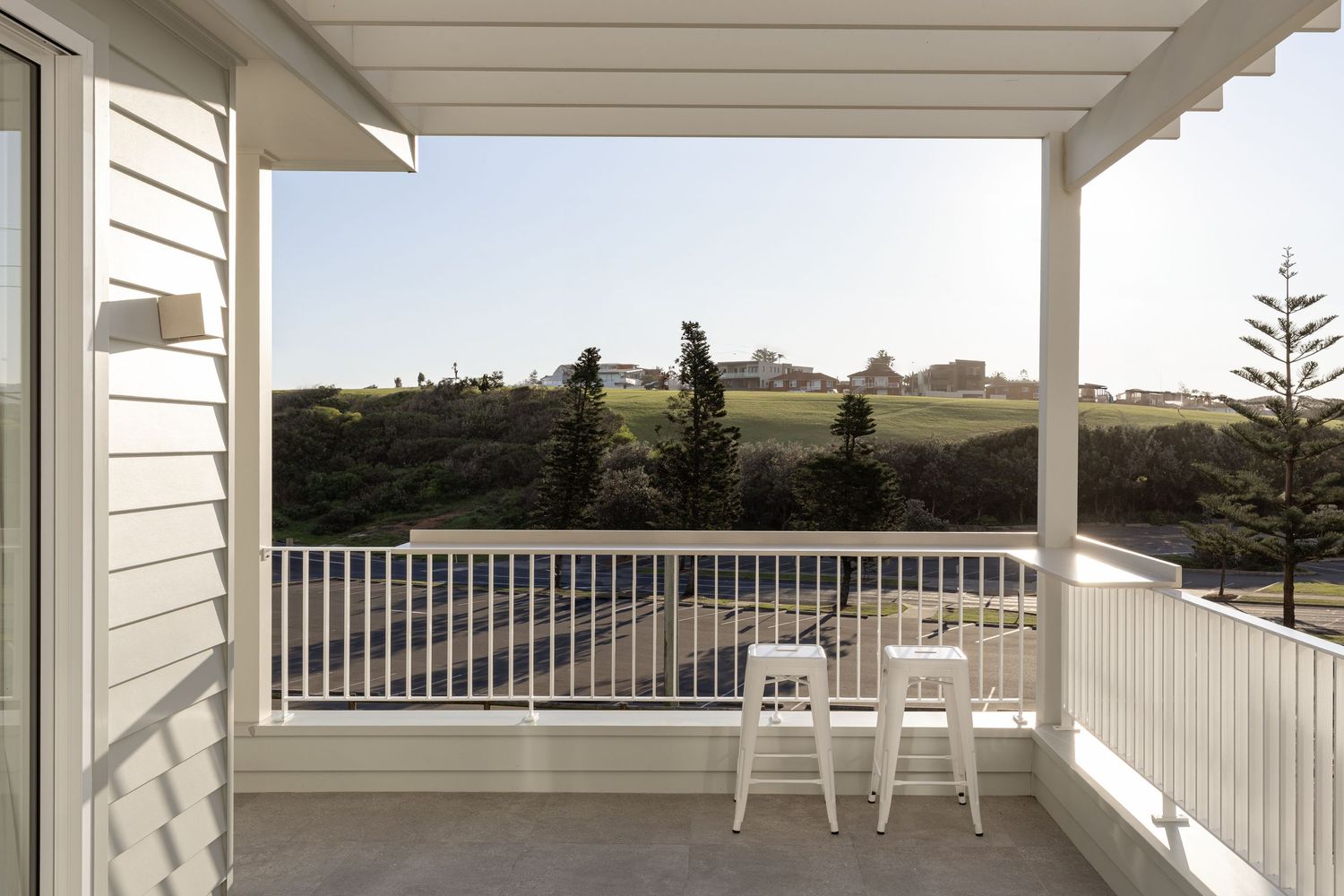 A serene white porch with Adirondack chairs overlooking rolling hills and distant trees on a sunny day.