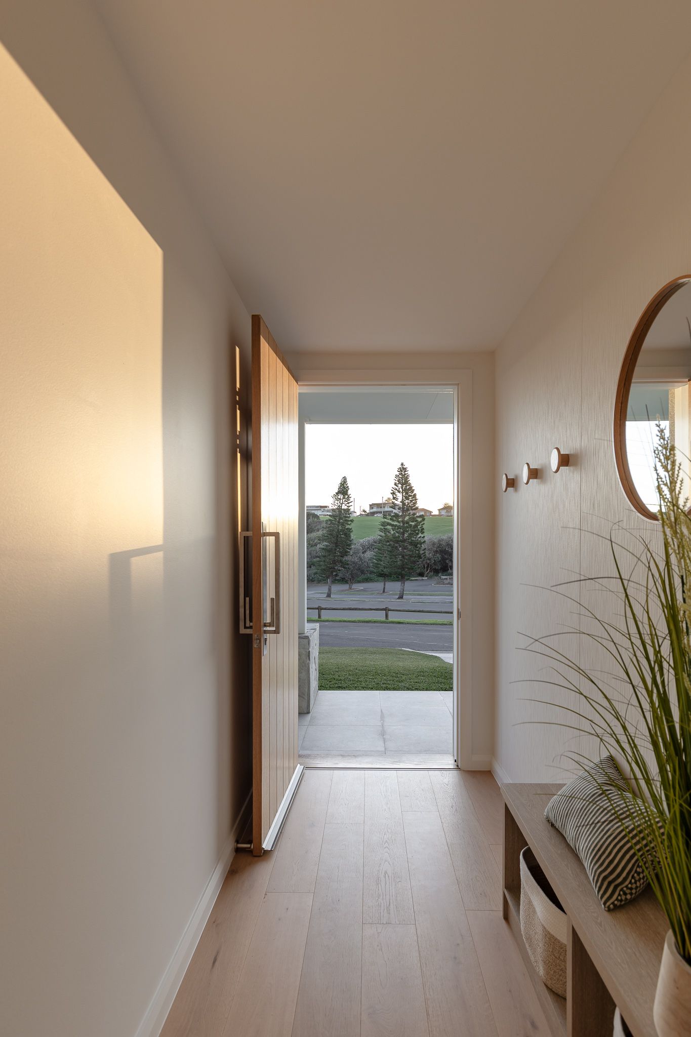 Minimalist white hallway with natural light streaming in and decorative potted plants along the wall.