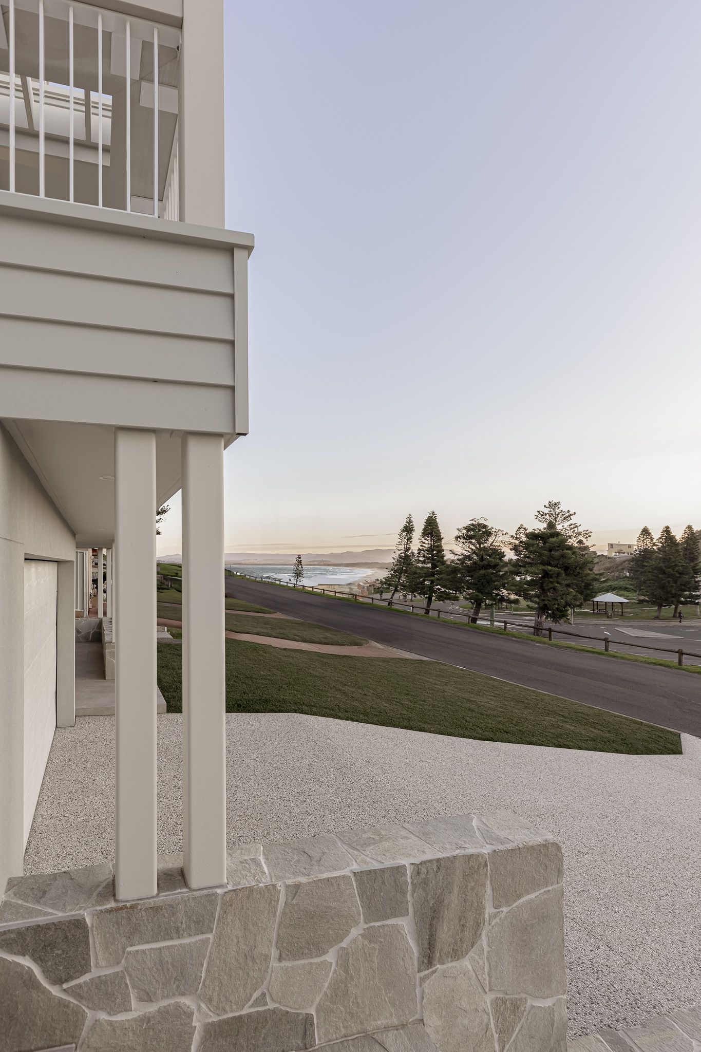 White pillared porch with stone foundation overlooking a grassy hillside and distant ocean view.
