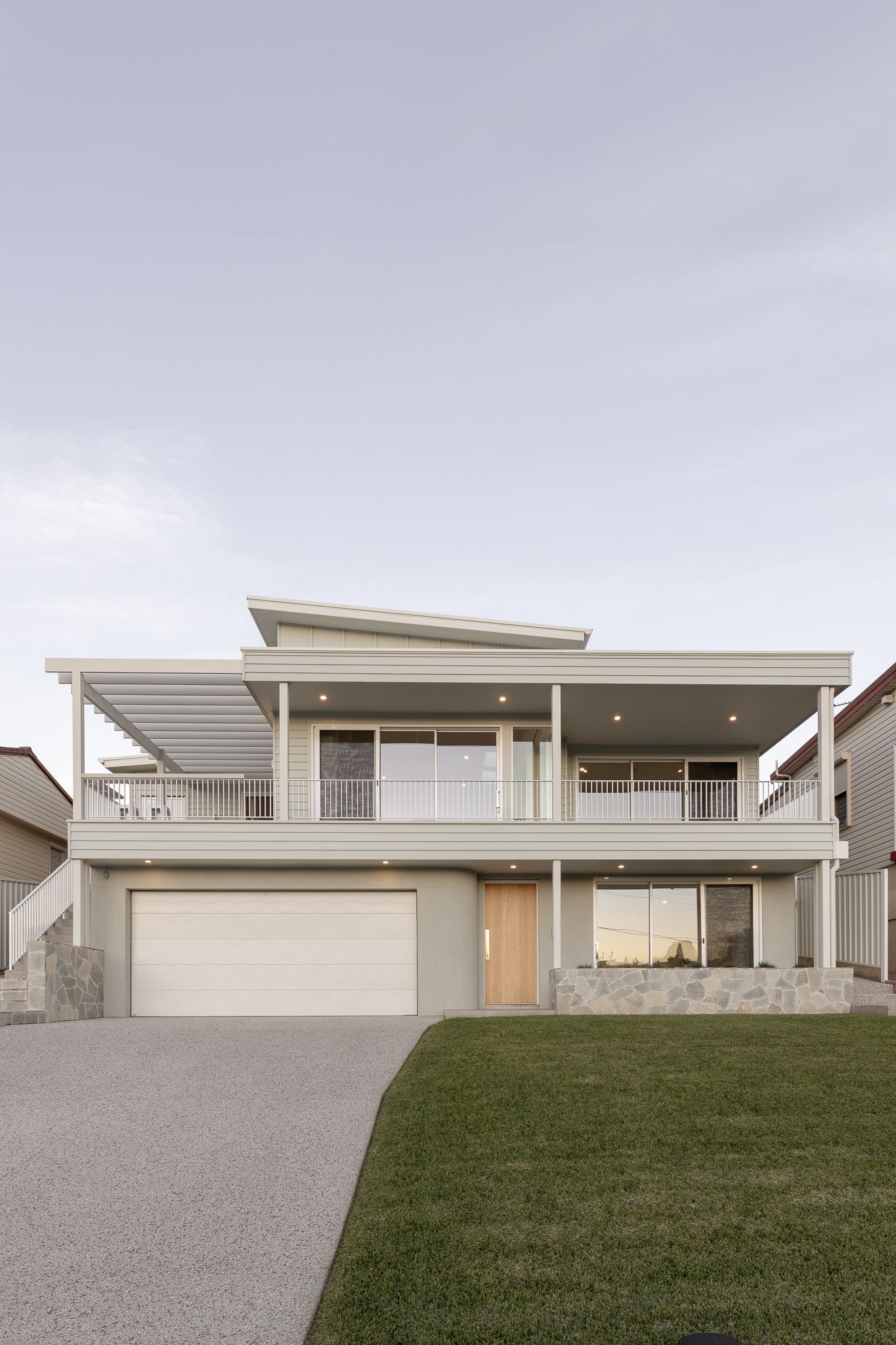 Contemporary coastal home featuring clean lines, glass railings and neutral tones against an overcast sky.