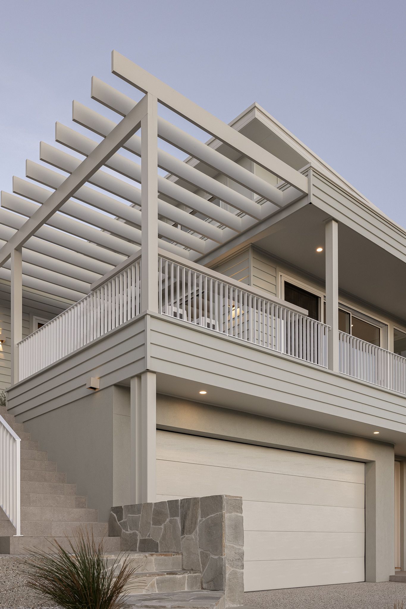 Contemporary white house exterior featuring pergola details and garage with stone accents.
