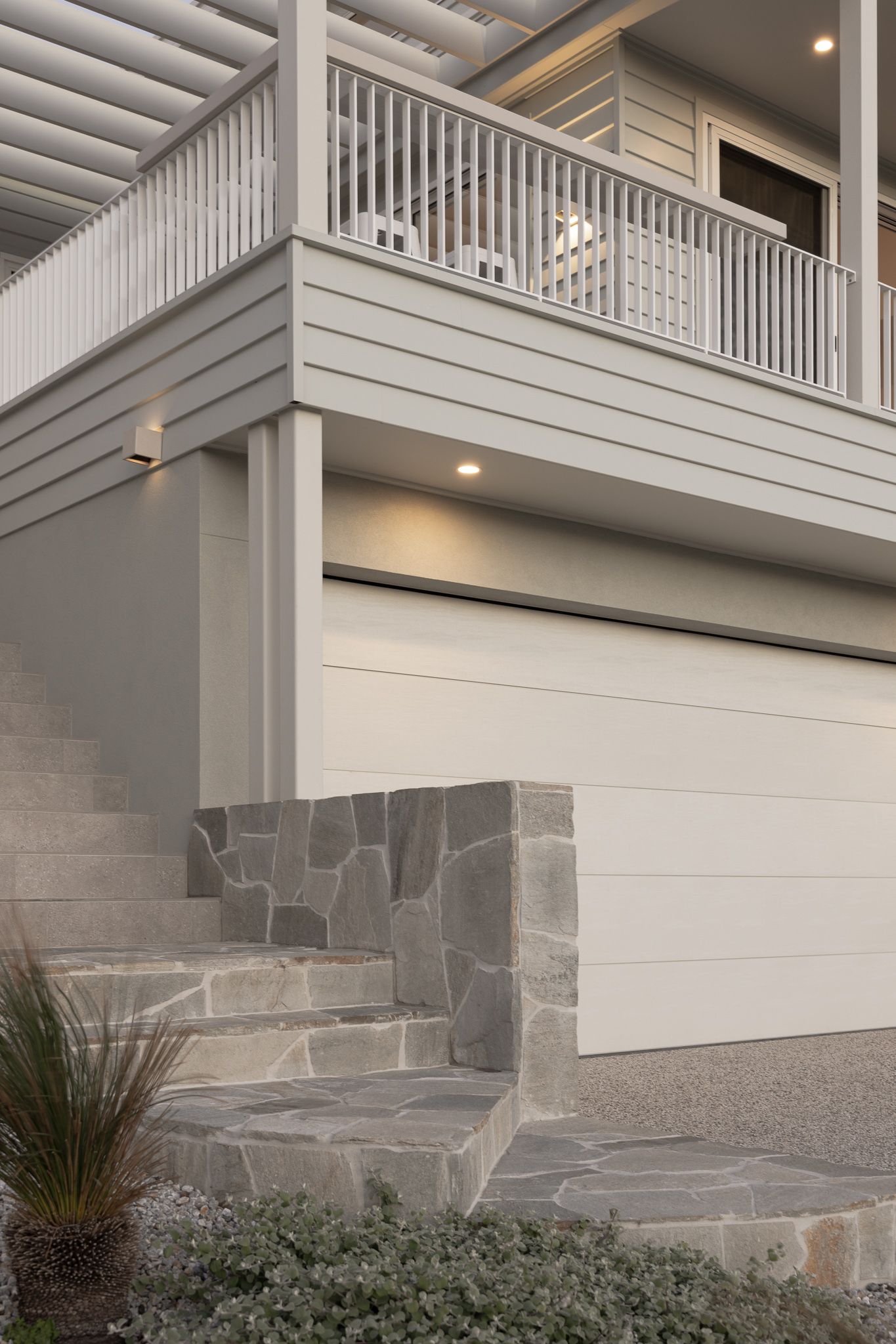 Modern home facade with stone retaining walls, white garage door, and architectural pergola details.