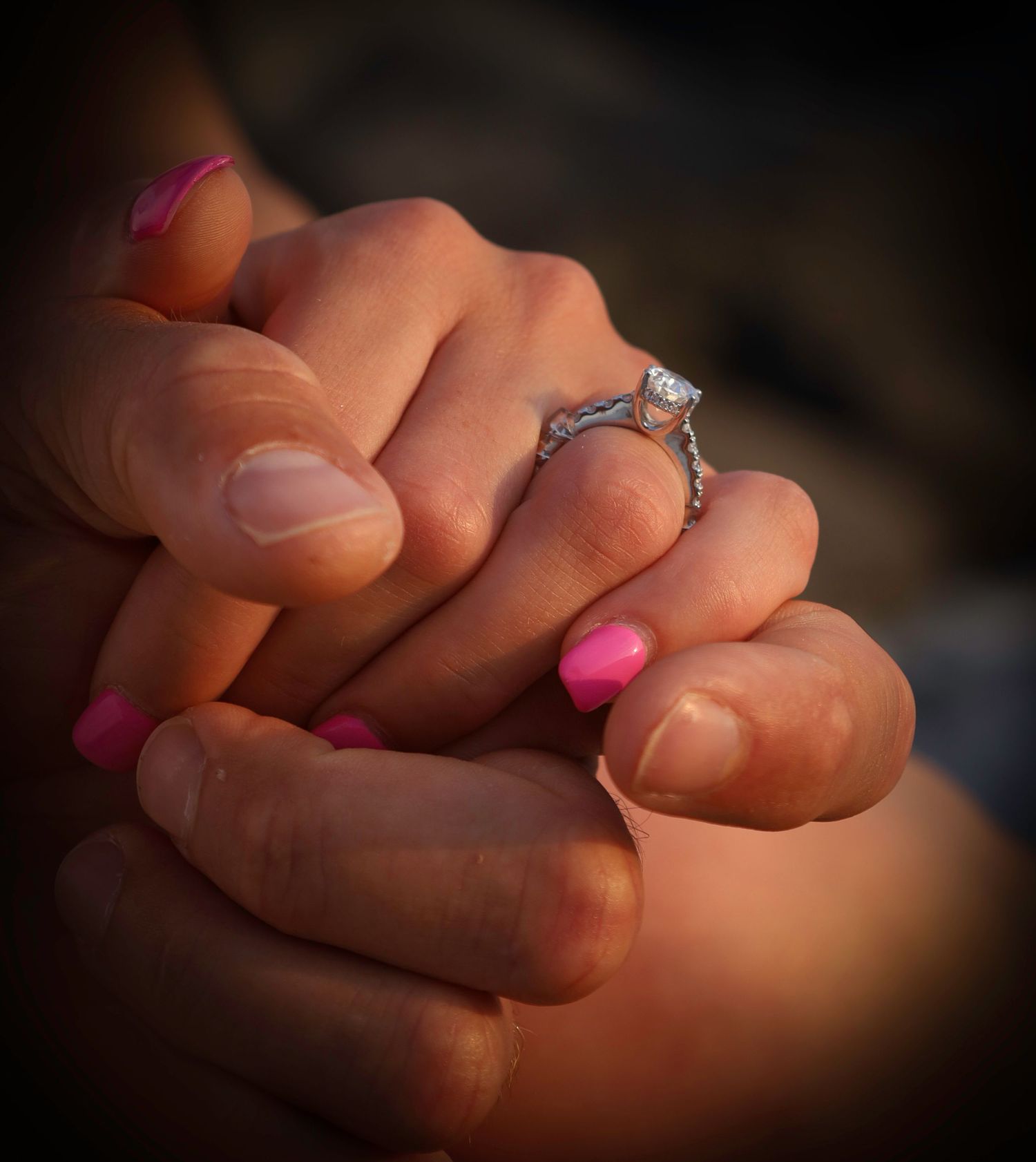Close-up sequence showing an engagement ring being placed on a hand with bright pink nail polish.