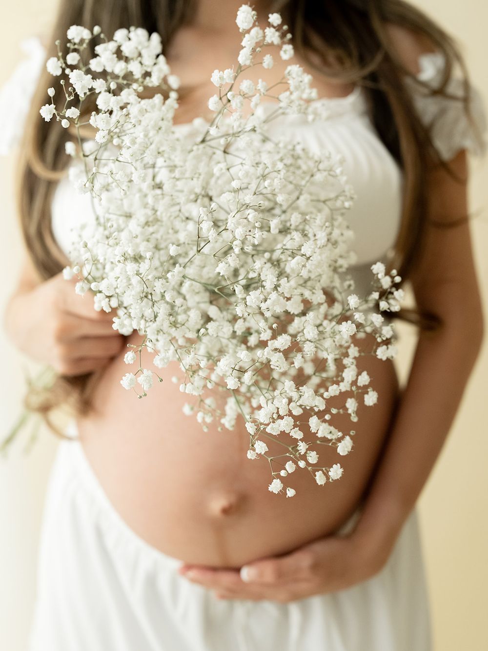 Delicate white baby's breath flowers held against a pregnant belly in a soft maternity photo.