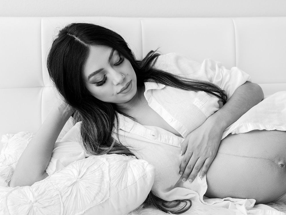 Peaceful black and white maternity photo captures relaxed moment on white bedding.