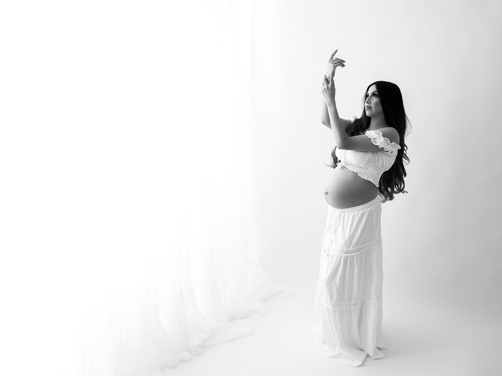 A figure in a white dress poses gracefully against a minimalist white background in an artistic fashion portrait series.