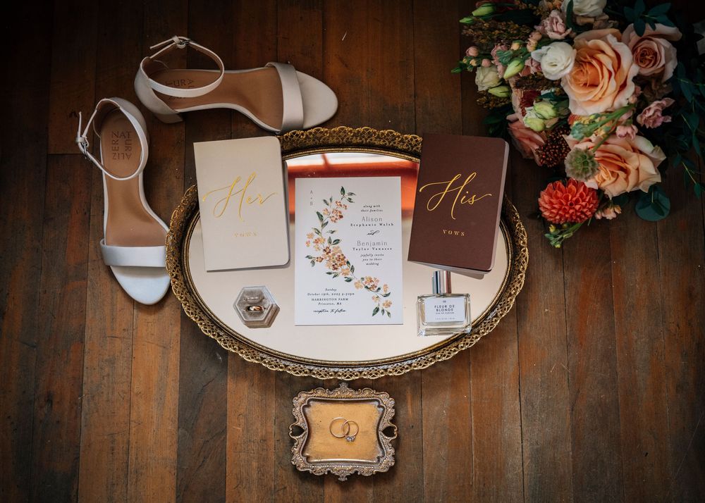 Wedding accessories including shoes, invitations, and floral details arranged on an antique mirrored tray.