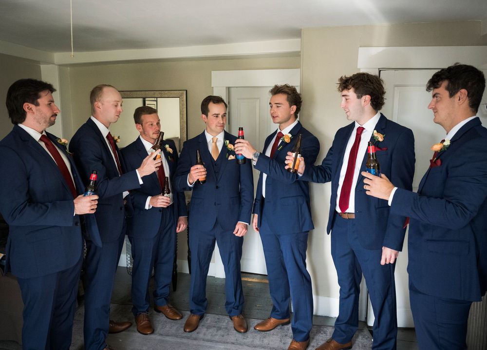 Groomsmen in navy suits gather for pre-wedding celebrations in a bright room.