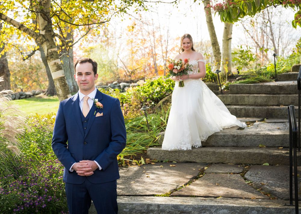 Wedding couple poses in front of stone steps and autumn foliage in an outdoor garden setting.