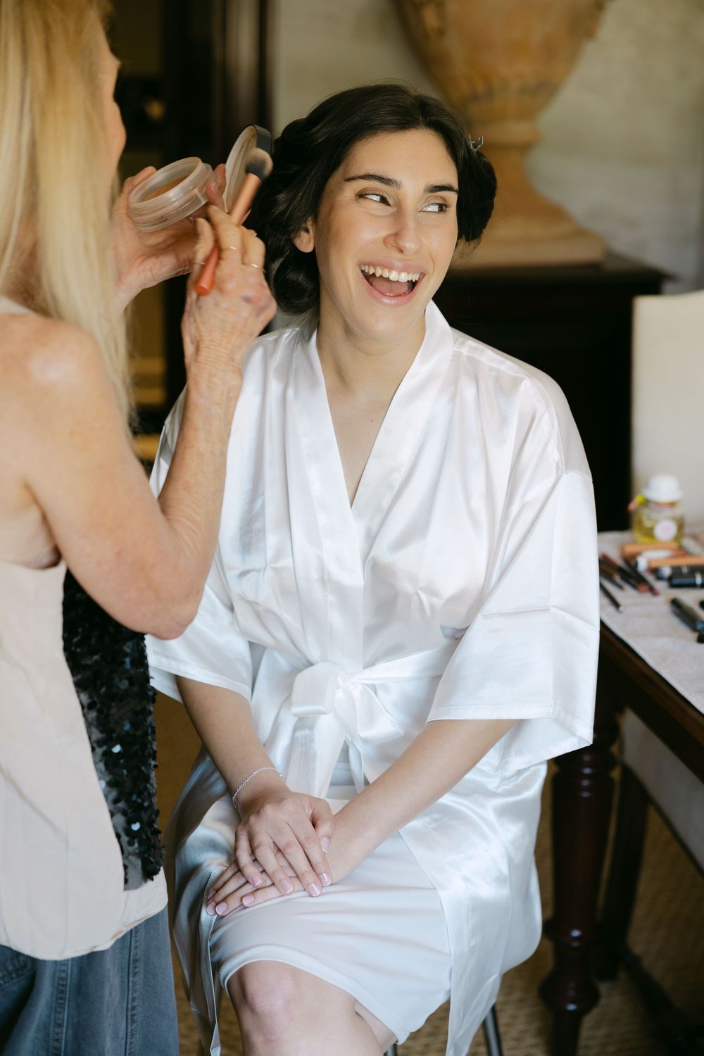 A person in a white silk robe smiles while getting their hair styled during preparation for a special event.
