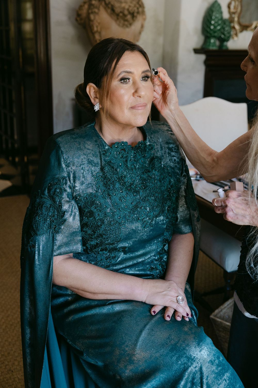 Person in a shimmering teal formal dress sits while getting ready for a special occasion.