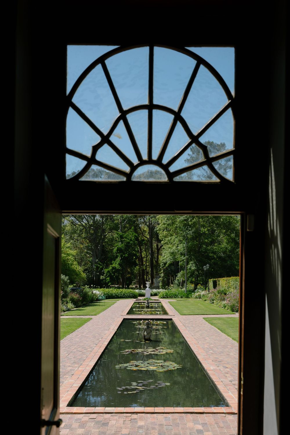A garden view through an arched window frame shows a reflecting pool and symmetrical landscaping.