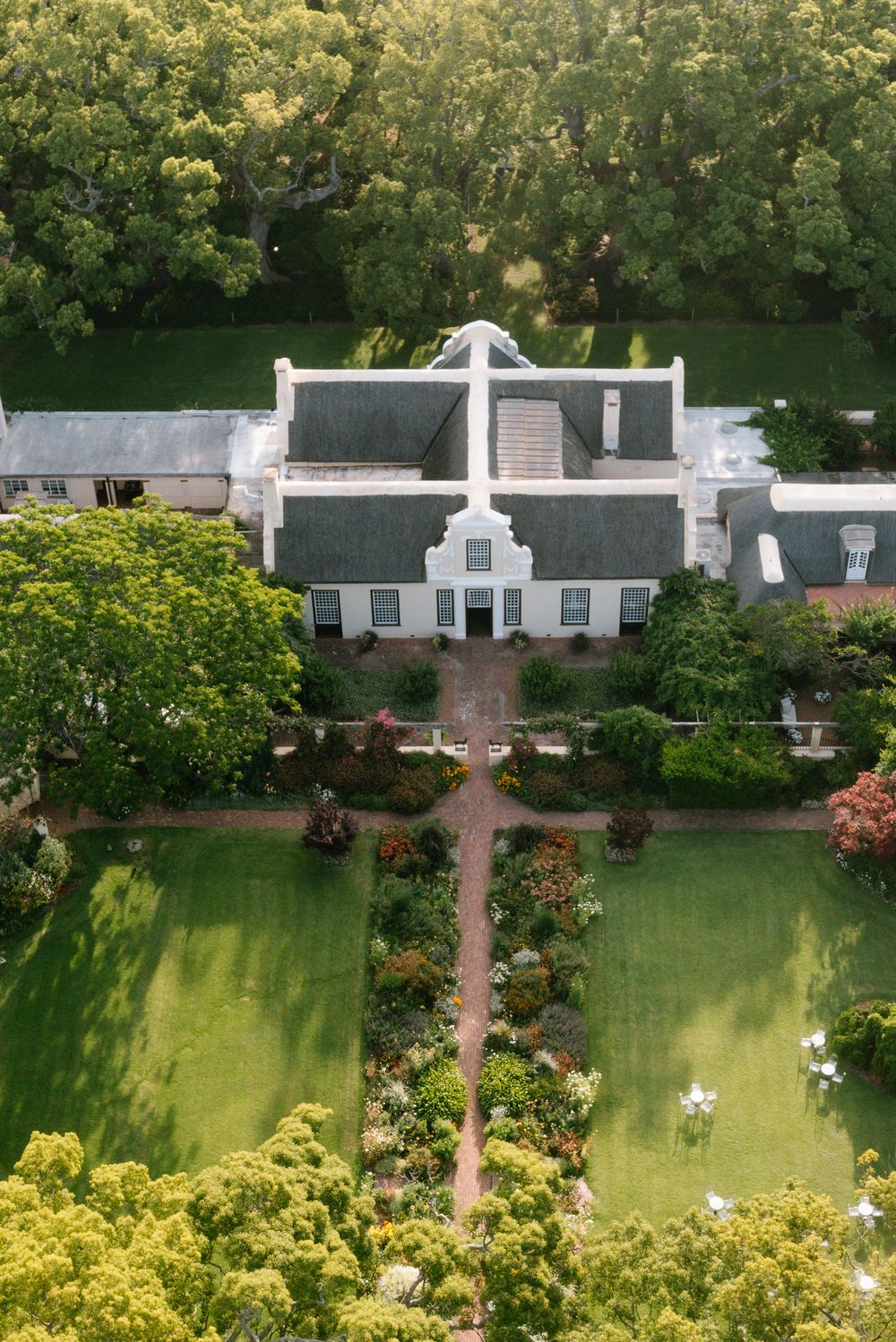 A scenic garden landscape with white architectural elements and lush green lawns bordered by flowering shrubs.