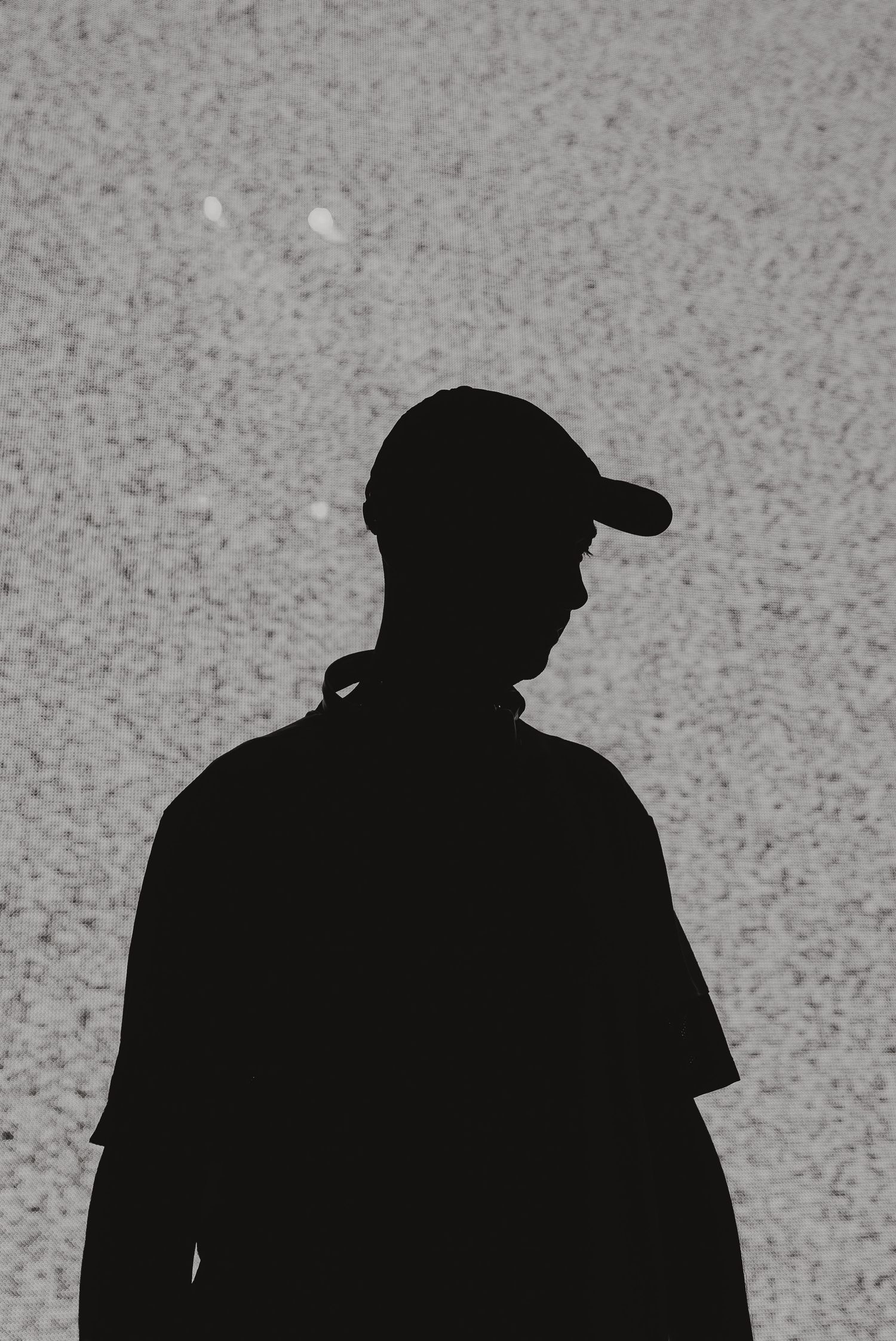 Black and white silhouette of person wearing baseball cap against textured background.