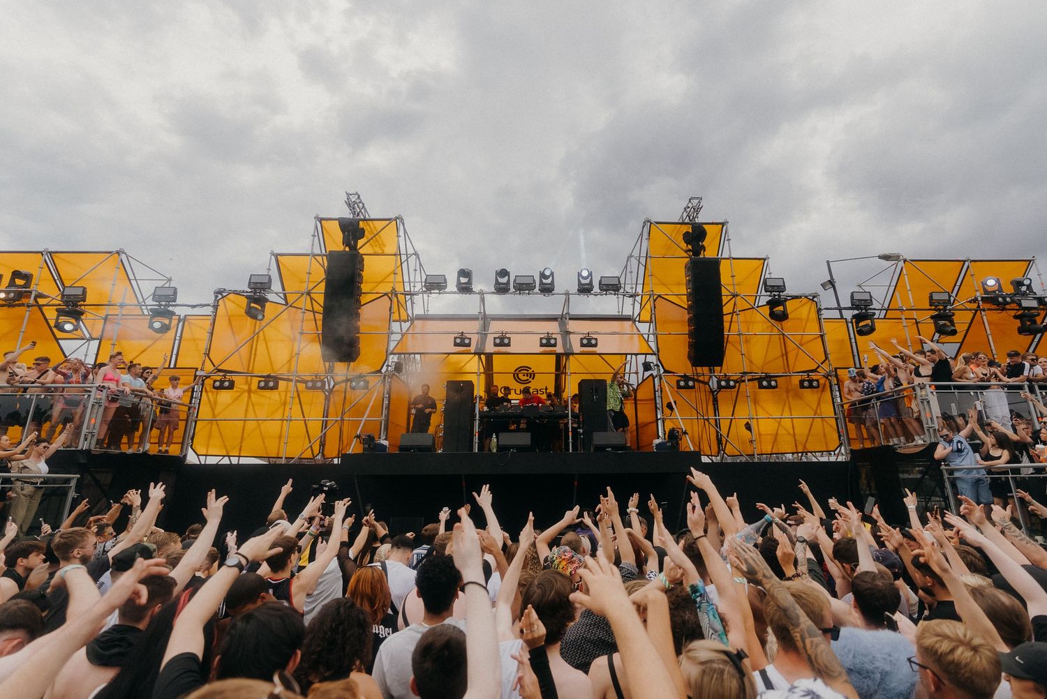 Yellow festival stage with crowd raising hands during outdoor music performance.