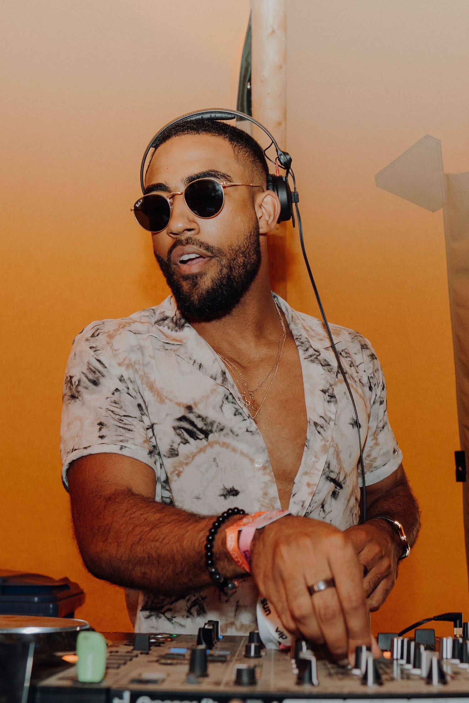 DJ in sunglasses and floral shirt mixing music at outdoor event.