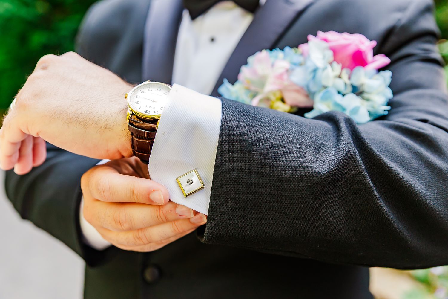A close-up view of hands holding a boutonniere pin during a formal event preparation.