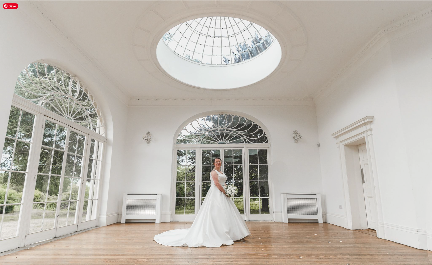 A light-filled conservatory with arched windows and a domed skylight features white decor and hardwood floors.