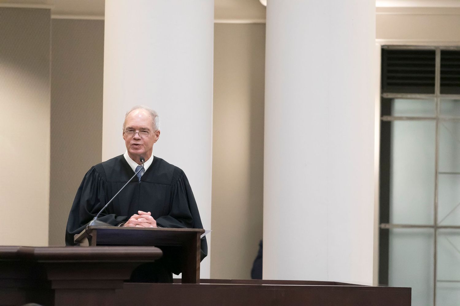 A judge in a black robe presides over court proceedings from behind a wooden bench.