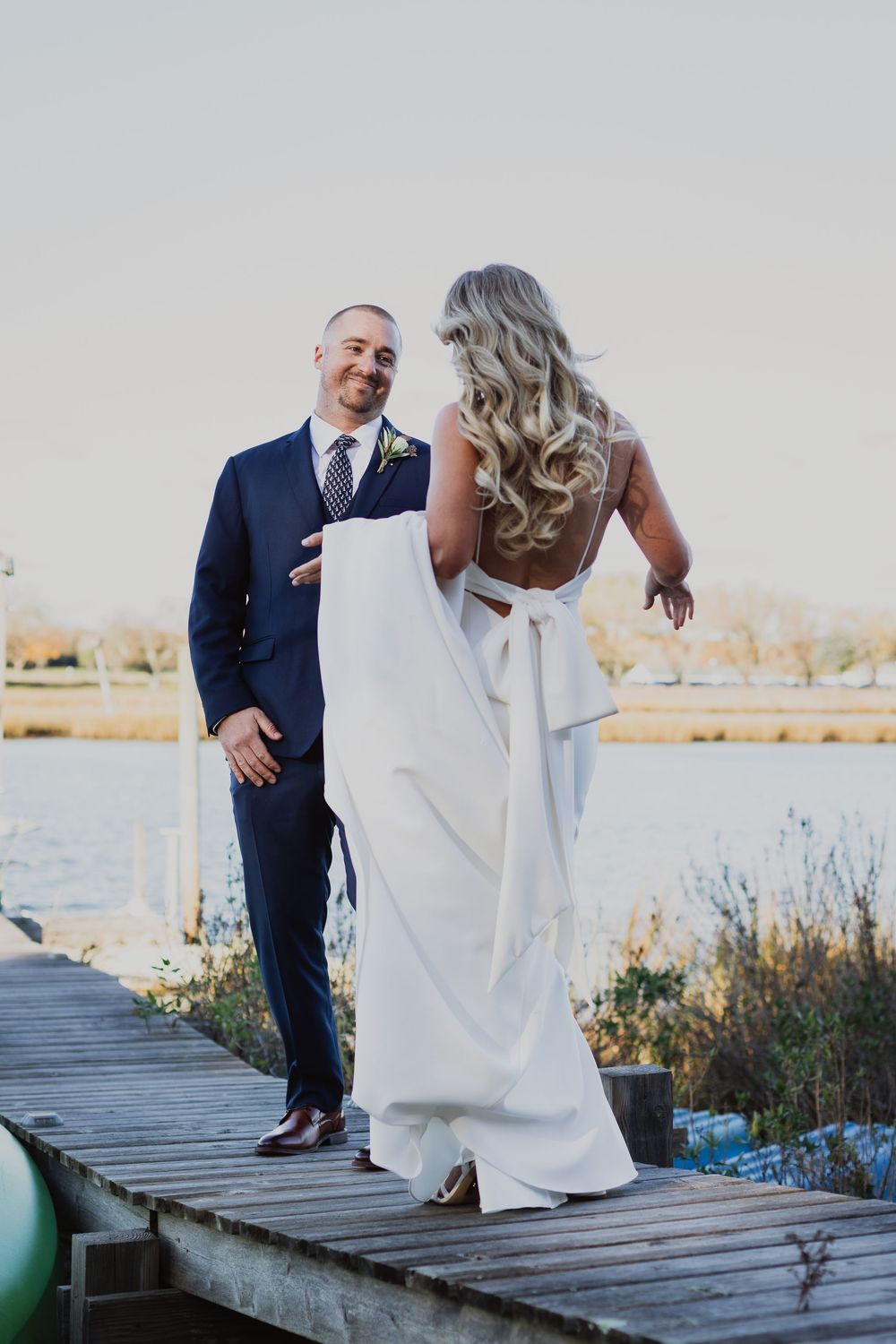Bride and groom share playful moments on a wooden dock by the water during their wedding photoshoot.