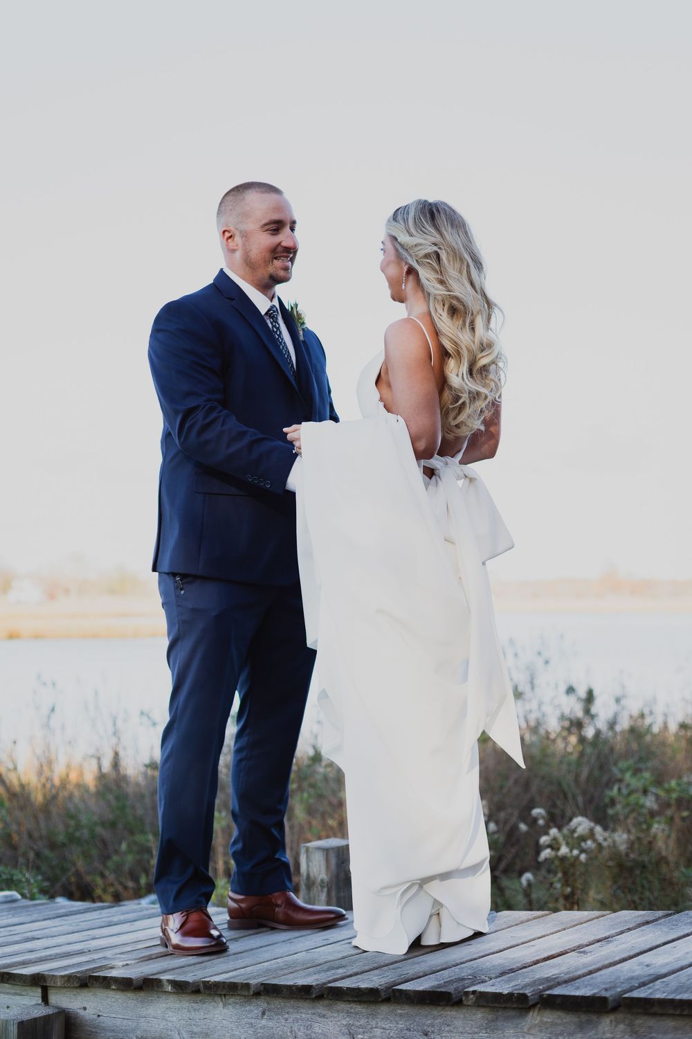 Wedding couple poses intimately on rustic boardwalk with water and natural scenery in background.