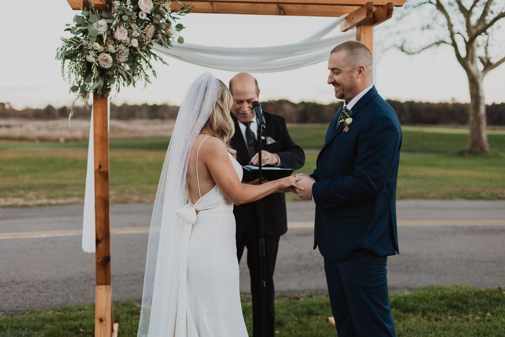 A couple shares a romantic moment during their outdoor wedding ceremony under a rustic wooden arch.