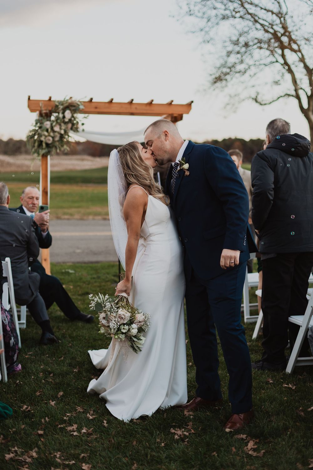 A romantic outdoor wedding ceremony sequence shows a couple sharing their first kiss under a wooden arbor.