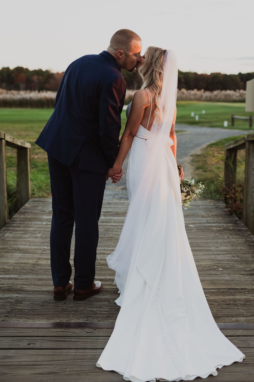 A romantic wedding couple shares an intimate moment on a wooden dock at sunset.