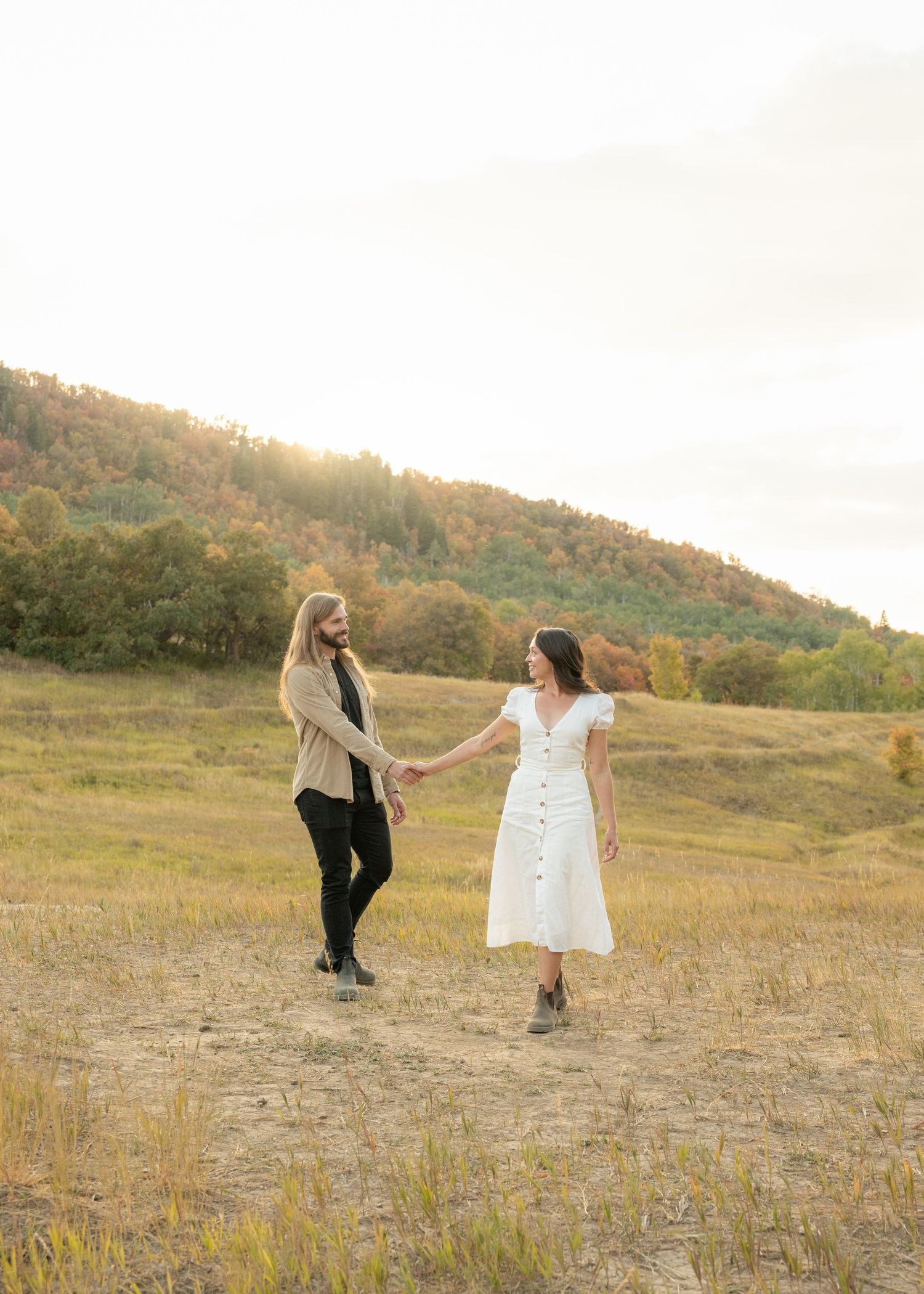 Two people dance and twirl together in a golden field at sunset with rolling hills in the background.