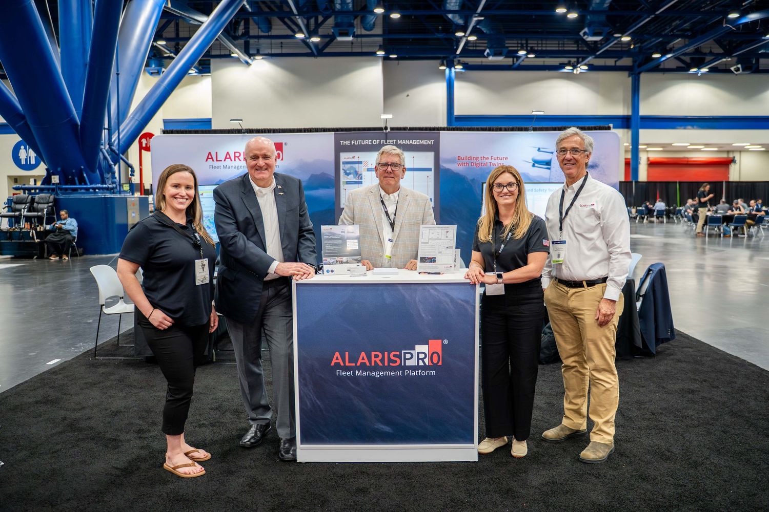 People networking and interacting at a business trade show with exhibition booths and displays visible in the background.