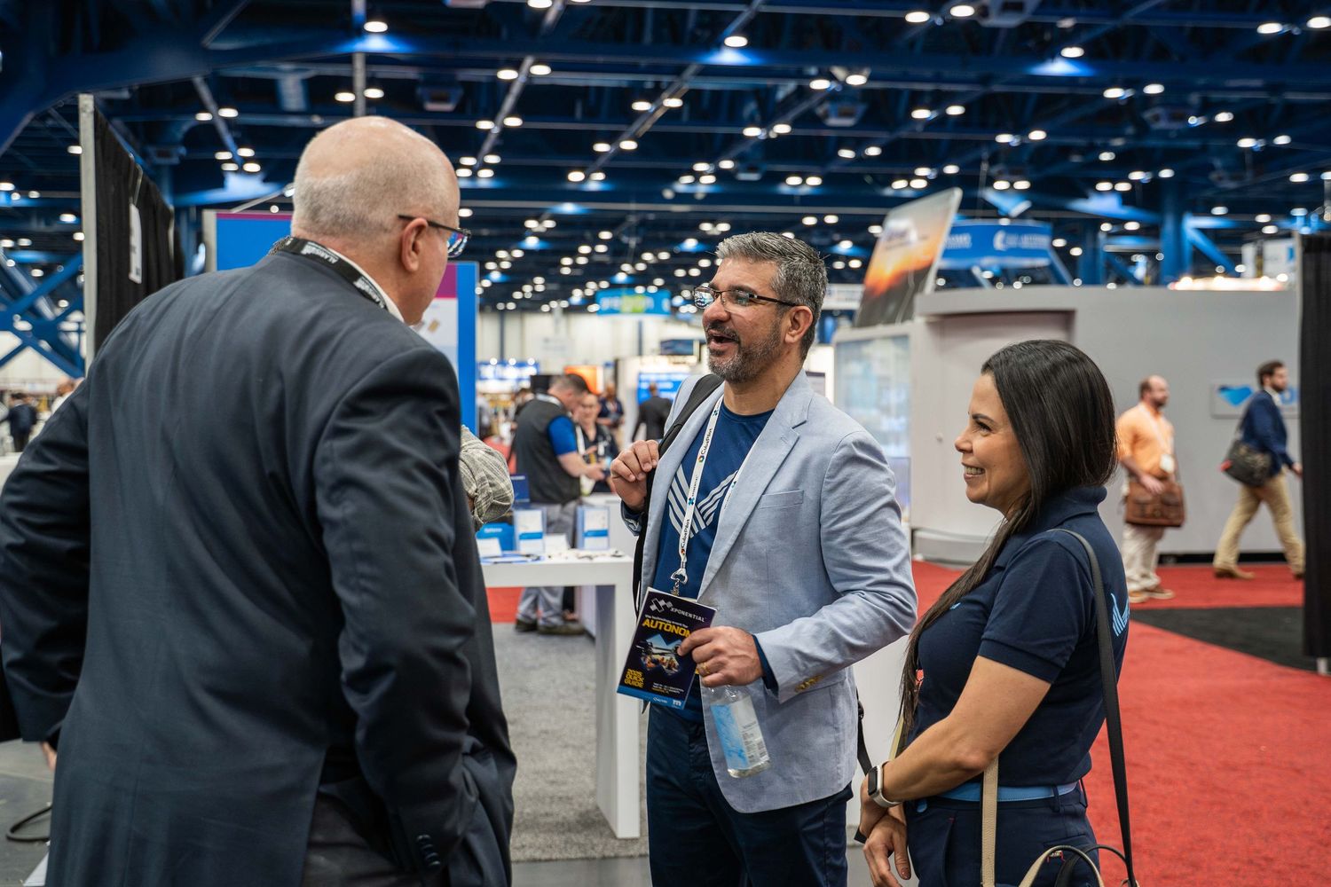 People networking and engaging in conversations at a business conference trade show floor with exhibition booths visible.