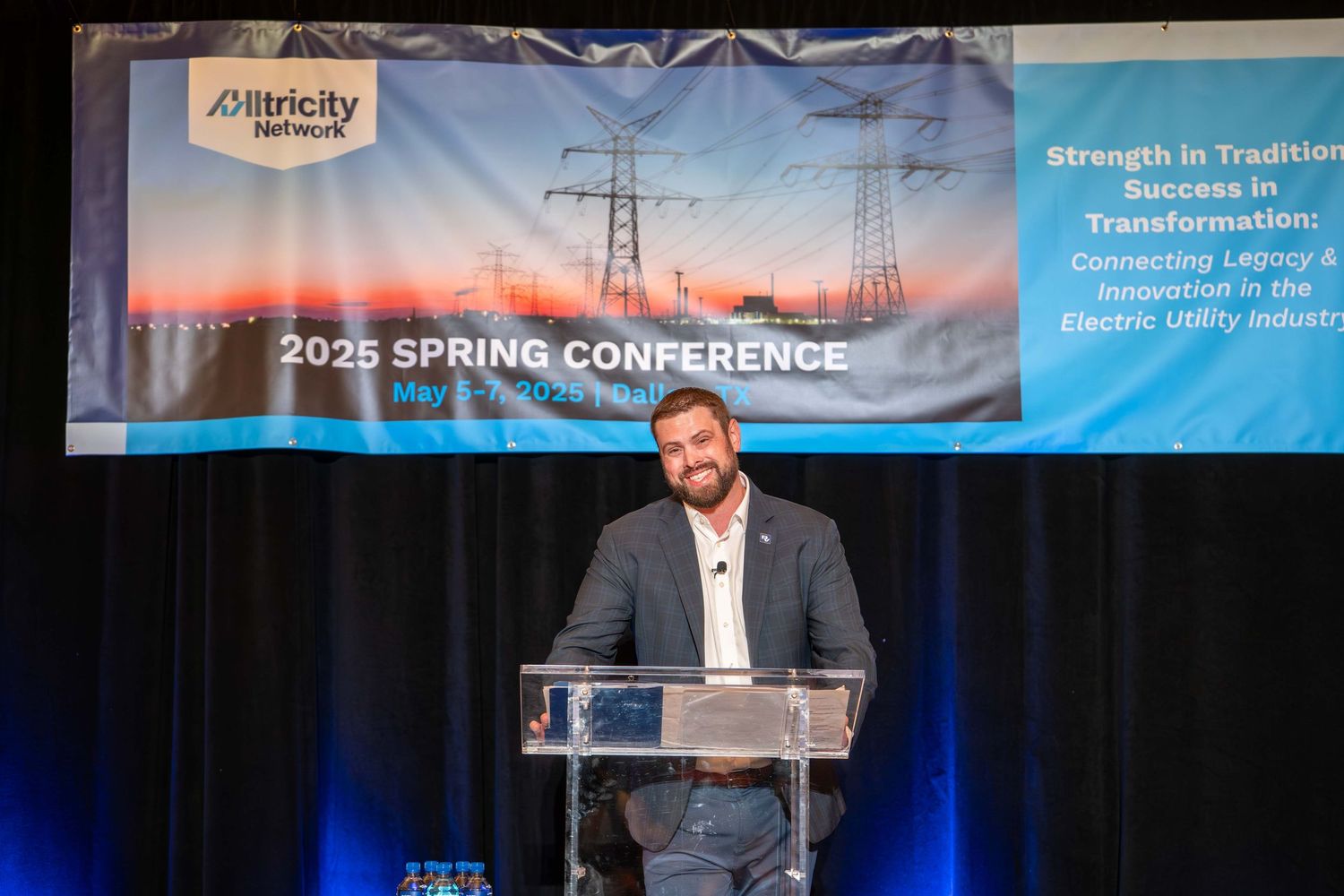 Speaker presenting on stage at a conference with blue banners and professional lighting setup.