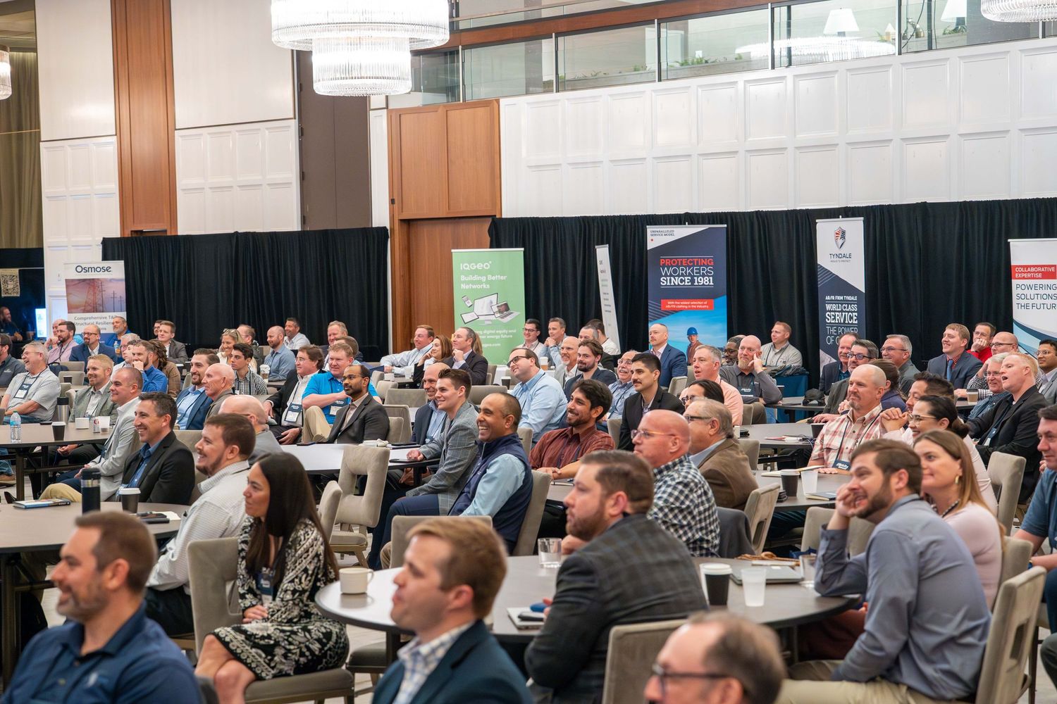Conference attendees listen attentively in a packed meeting room during a professional presentation.