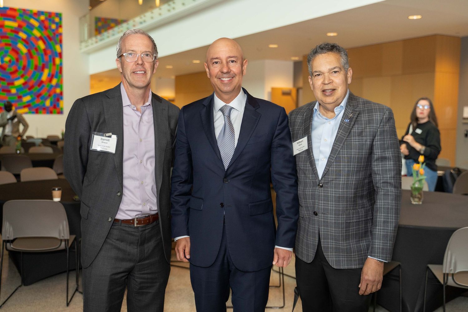 Three business professionals in formal attire pose together at a corporate networking event.
