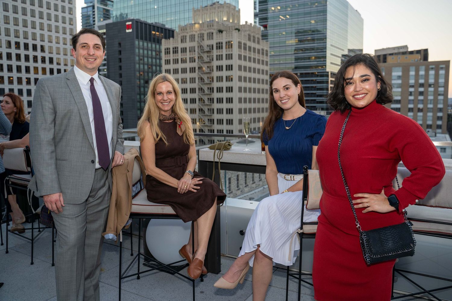 Business professionals network and socialize at a rooftop event with city skyline views during sunset.