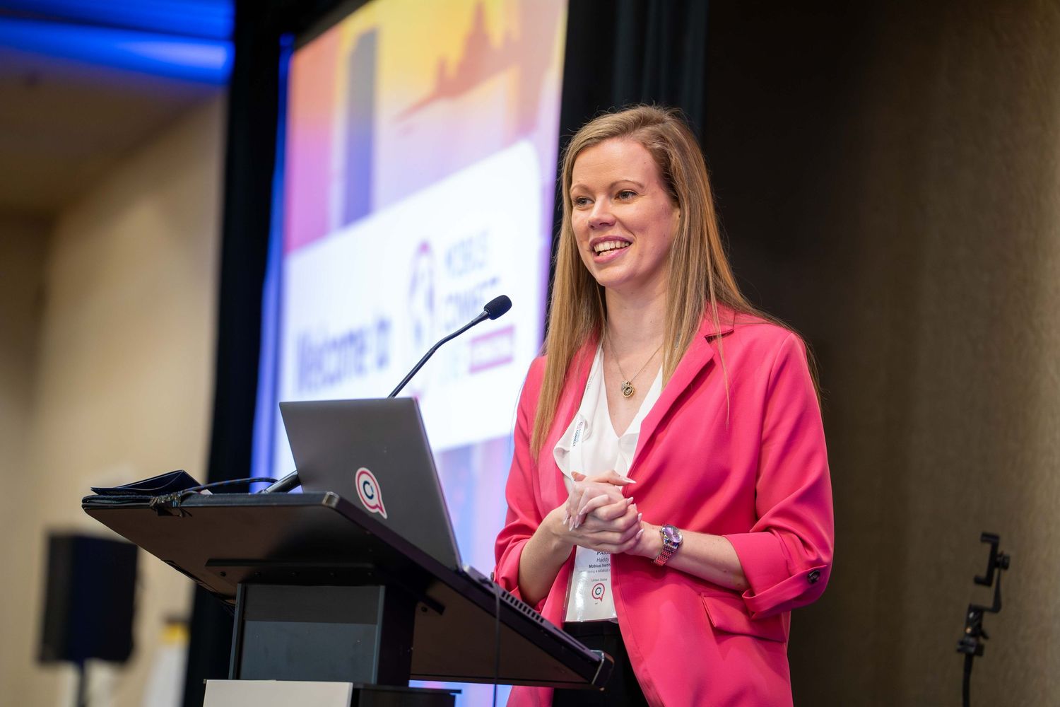 Speaker in bright pink blazer presenting at a professional conference podium.