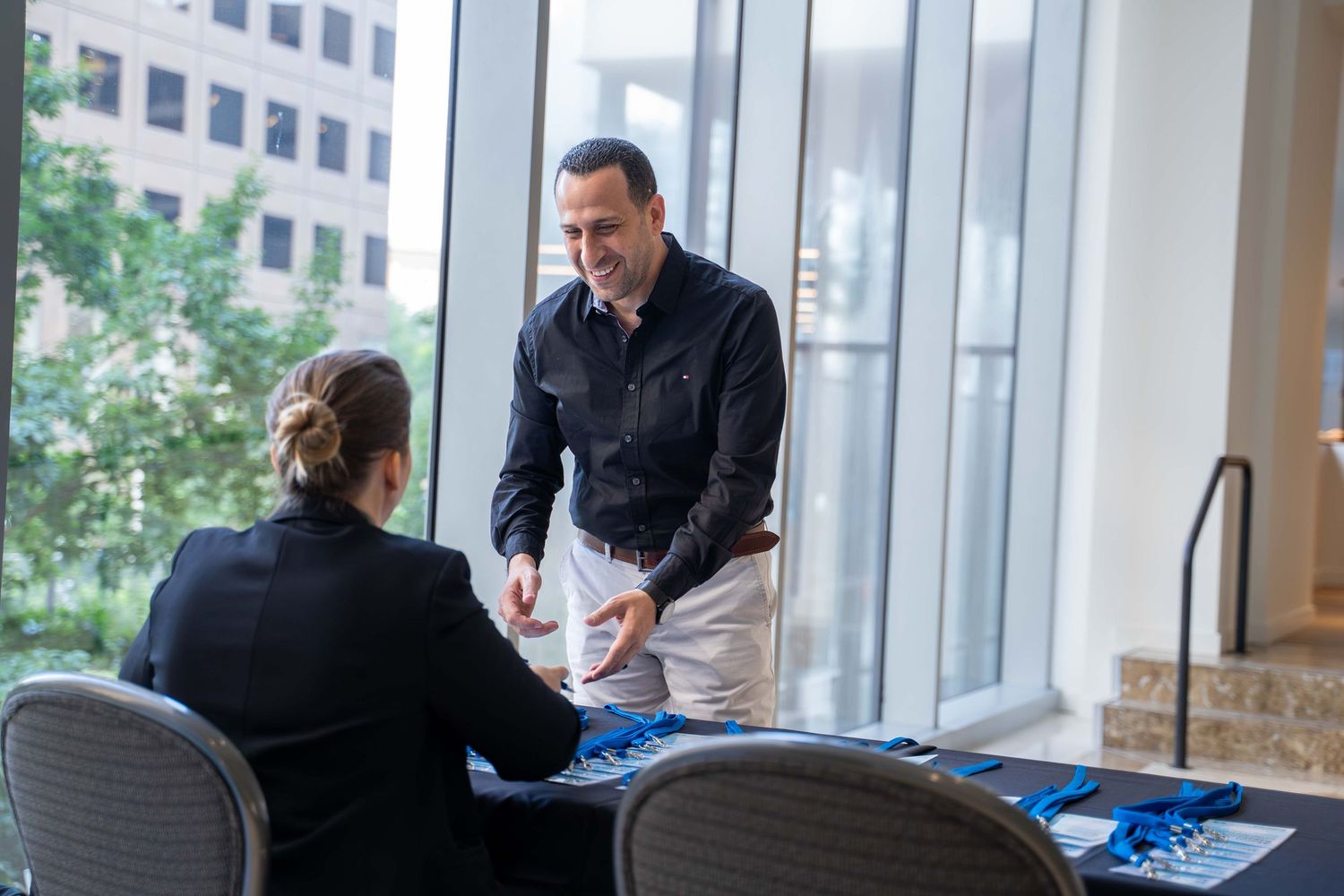 Professional networking event with attendees having discussions in a modern office space with large windows.