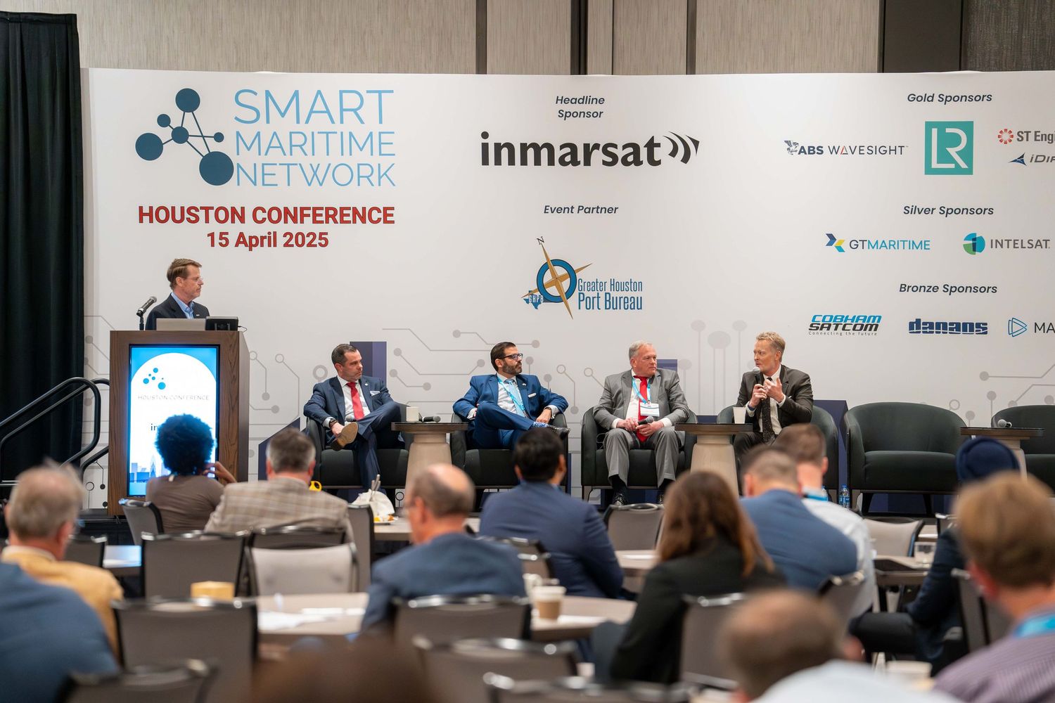 Panel discussion at Smart Solutions Houston Conference with speakers seated on stage in front of corporate sponsor banners.